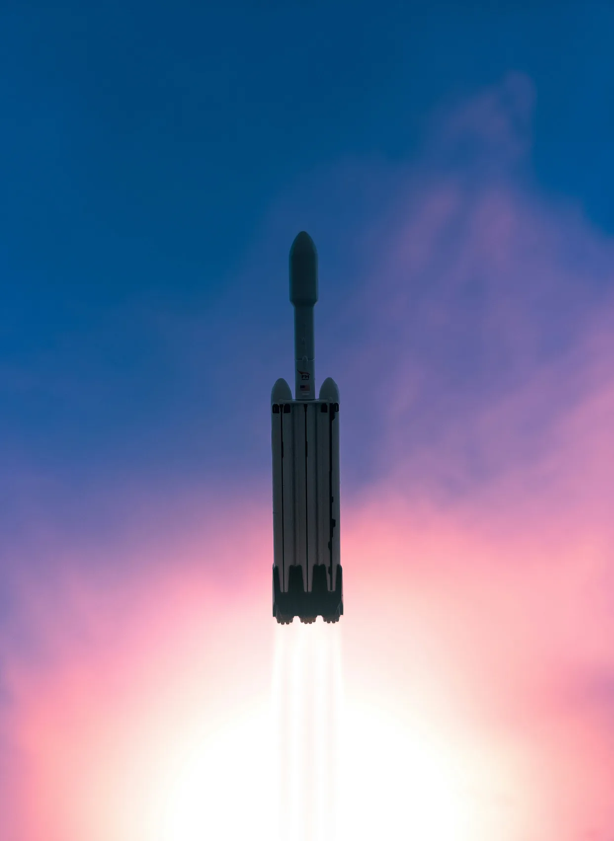 A rocket lifting off, seen against a blue-to-pink dusk sky.