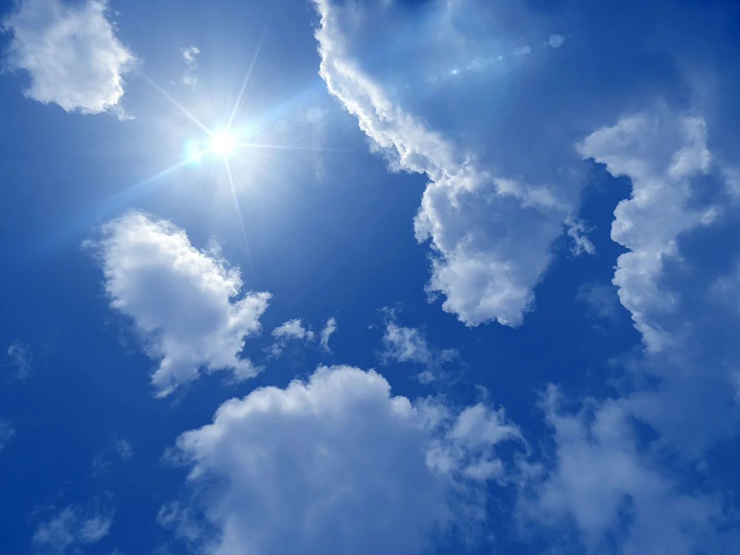 The sun flaring between cumulus clouds in a deep blue sky.