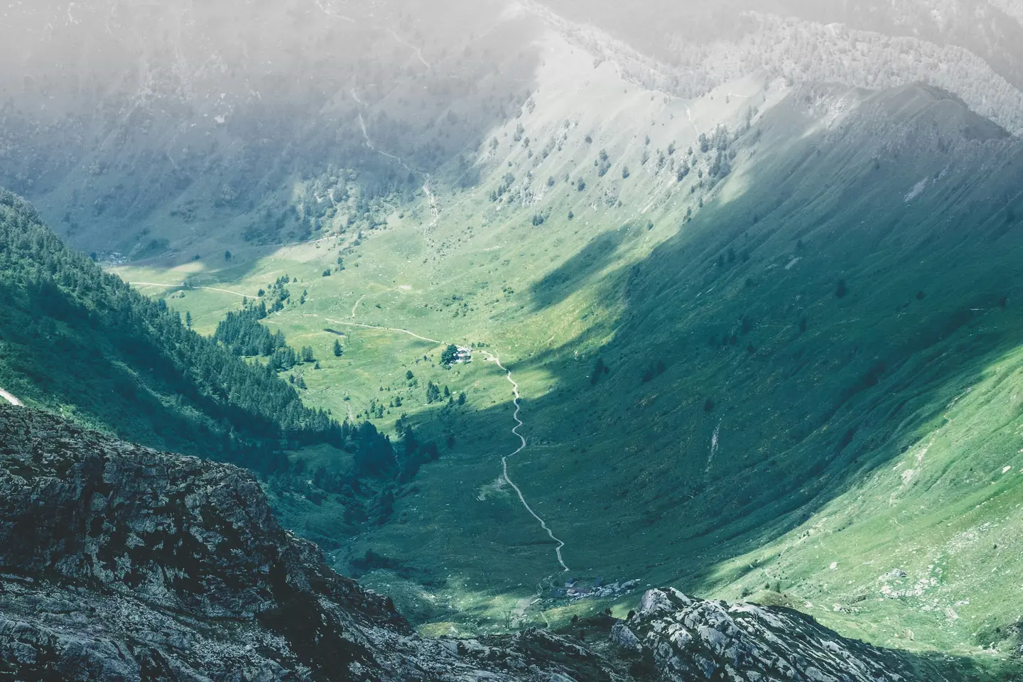 A green alpine valley in mist, a footpath winding up through it.